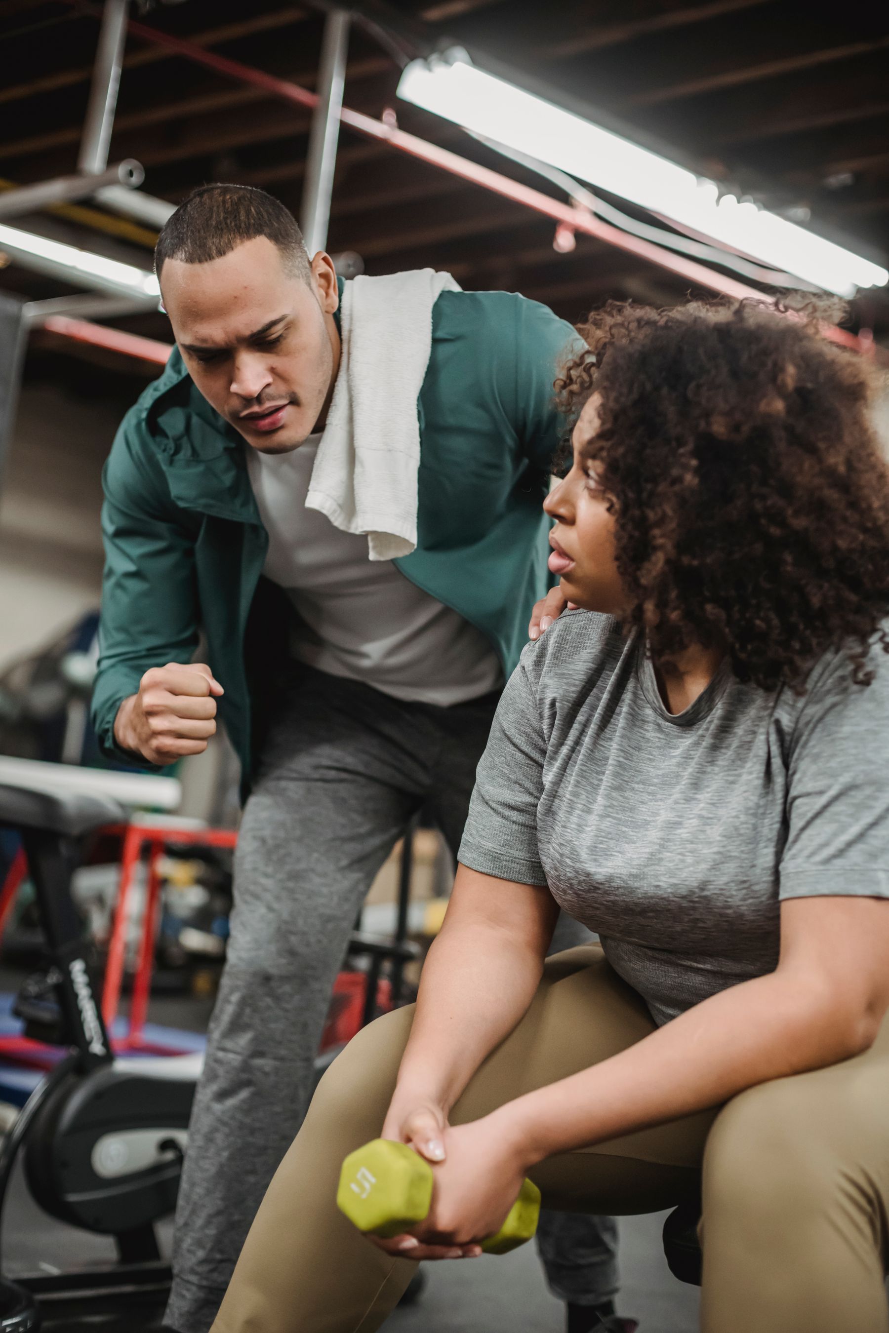 Trainer in a green coaching jacket supporting a client in the gym